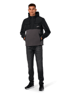 Veste Hybride Alpinestars Juncture, Noir et Anthracite, anorak à capuche en matériaux mixtes avec corps en polaire de toile et empiècements en ripstop, logo A-star blanc sur la poitrine, capuche avec cordon de serrage, portée par un mannequin avec un jean foncé et des baskets noires, streetwear décontracté inspiré du sport automobile