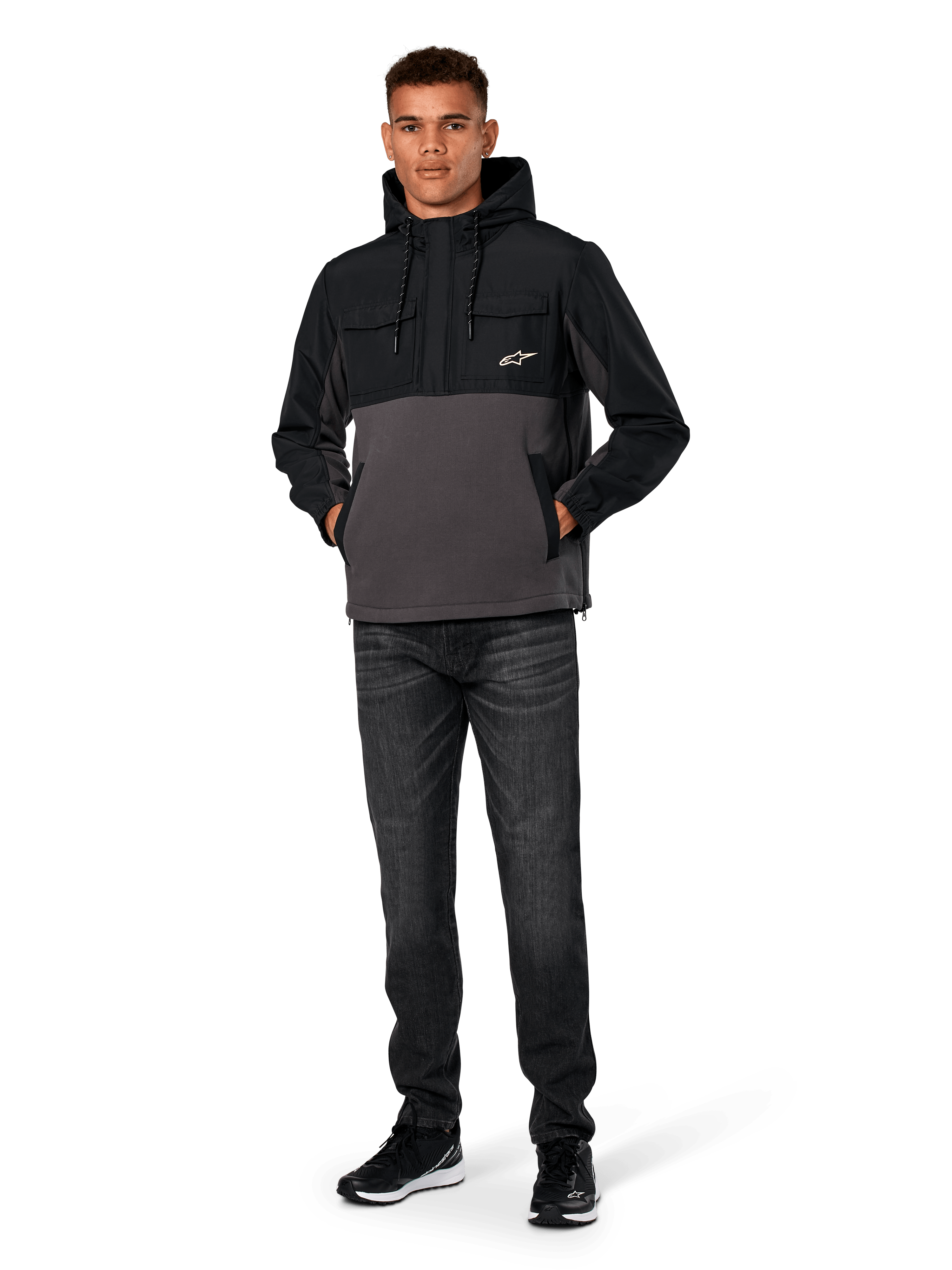 Veste Hybride Alpinestars Juncture, Noir et Anthracite, anorak à capuche en matériaux mixtes avec corps en polaire de toile et empiècements en ripstop, logo A-star blanc sur la poitrine, capuche avec cordon de serrage, portée par un mannequin avec un jean foncé et des baskets noires, streetwear décontracté inspiré du sport automobile