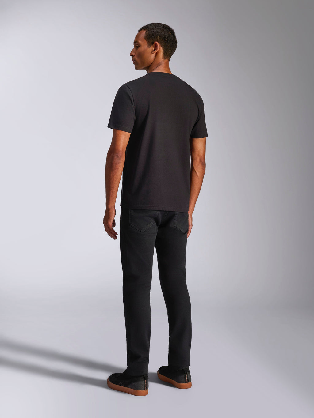 T-shirt Alpinestars Ageless 2.0 CSF, t-shirt à manches courtes, noir, vue de dos sur un mannequin homme, porté avec un pantalon noir et des baskets à semelles en gomme, style streetwear décontracté inspiré du sport automobile