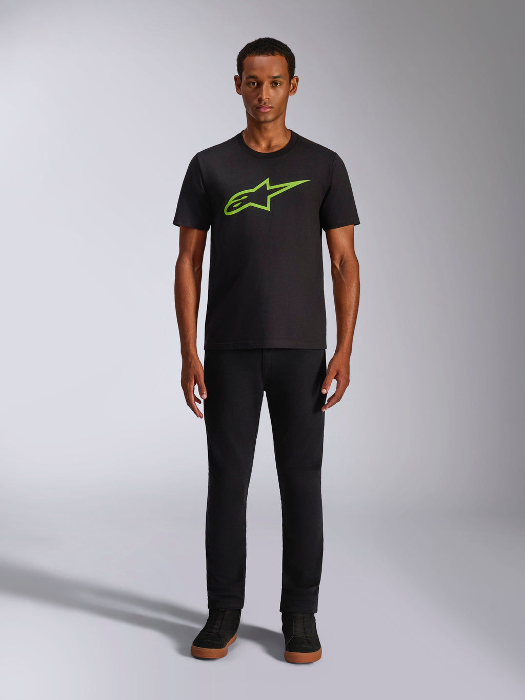 T-shirt Alpinestars Ageless 2.0 CSF, t-shirt à manches courtes, noir avec logo vert vif, porté par un mannequin avec un pantalon noir, design décontracté inspiré des sports mécaniques