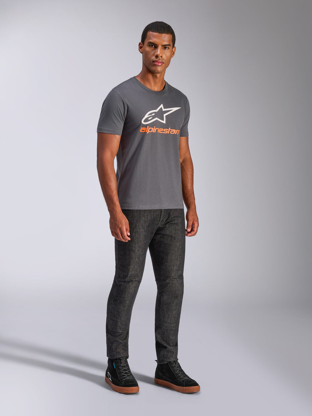 T-shirt Alpinestars Always 2.0 CSF, t-shirt à manches courtes, gris anthracite, logo A-star blanc avec marquage orange, style streetwear décontracté porté avec un jean foncé et des baskets noires