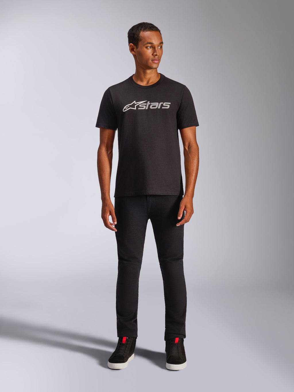 Alpinestars Blaze 2.0 CSF Tee, t-shirt à manches courtes, noir avec logo frontal gris et blanc, porté par un mannequin avec un pantalon noir et des chaussures noires, streetwear décontracté inspiré des sports mécaniques