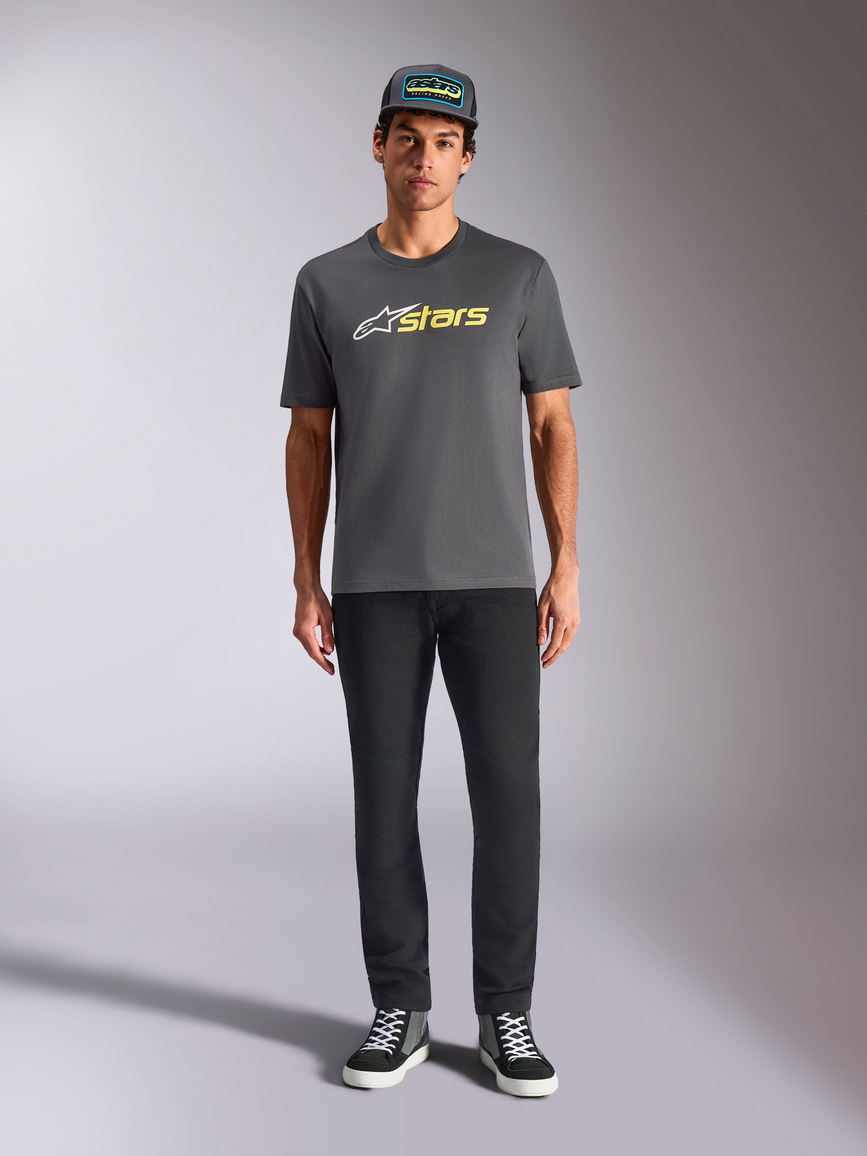 Tee-shirt Alpinestars Blaze 2.0 CSF, t-shirt à manches courtes, gris anthracite avec logo blanc et jaune fluo, porté avec un pantalon noir et une casquette trucker assortie, style motorsport décontracté