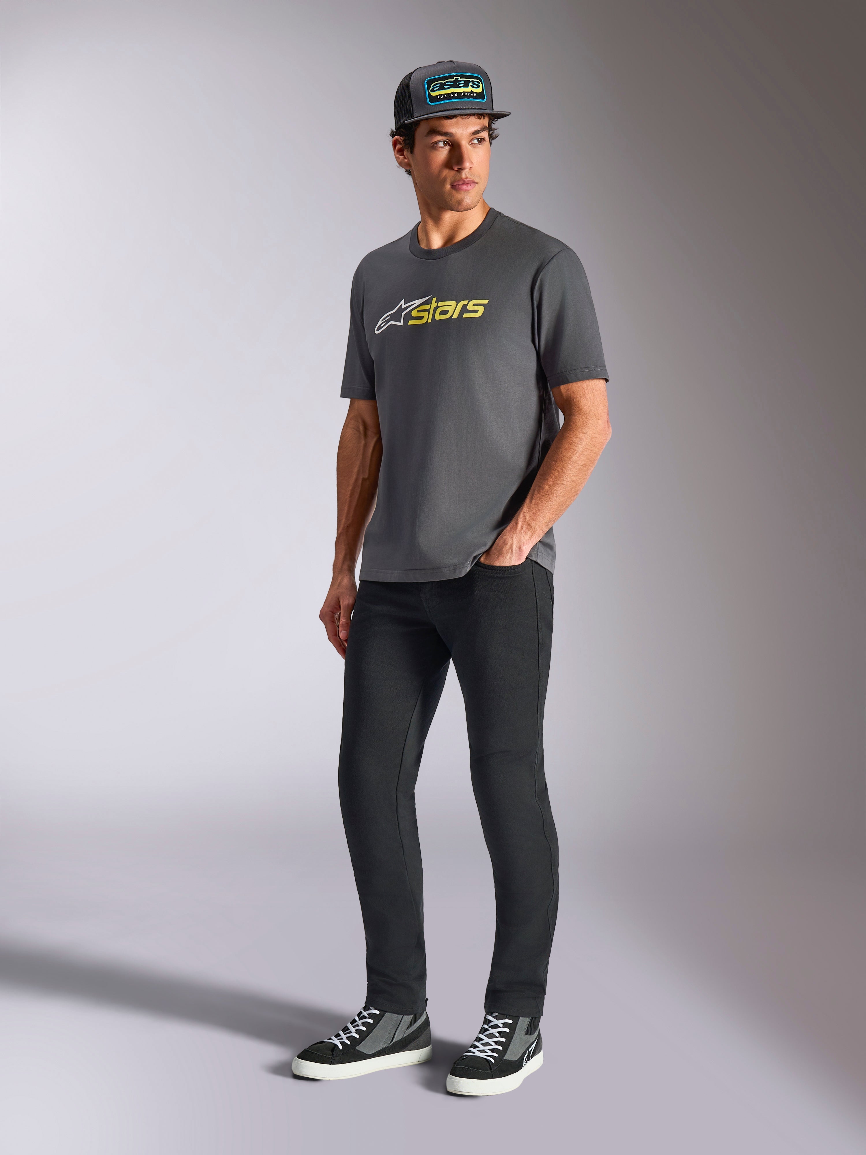T-shirt Alpinestars Blaze 2.0 CSF, t-shirt à manches courtes, gris anthracite avec logo blanc et jaune fluo, porté par un mannequin avec casquette et pantalon noirs, vêtement lifestyle décontracté inspiré des sports mécaniques