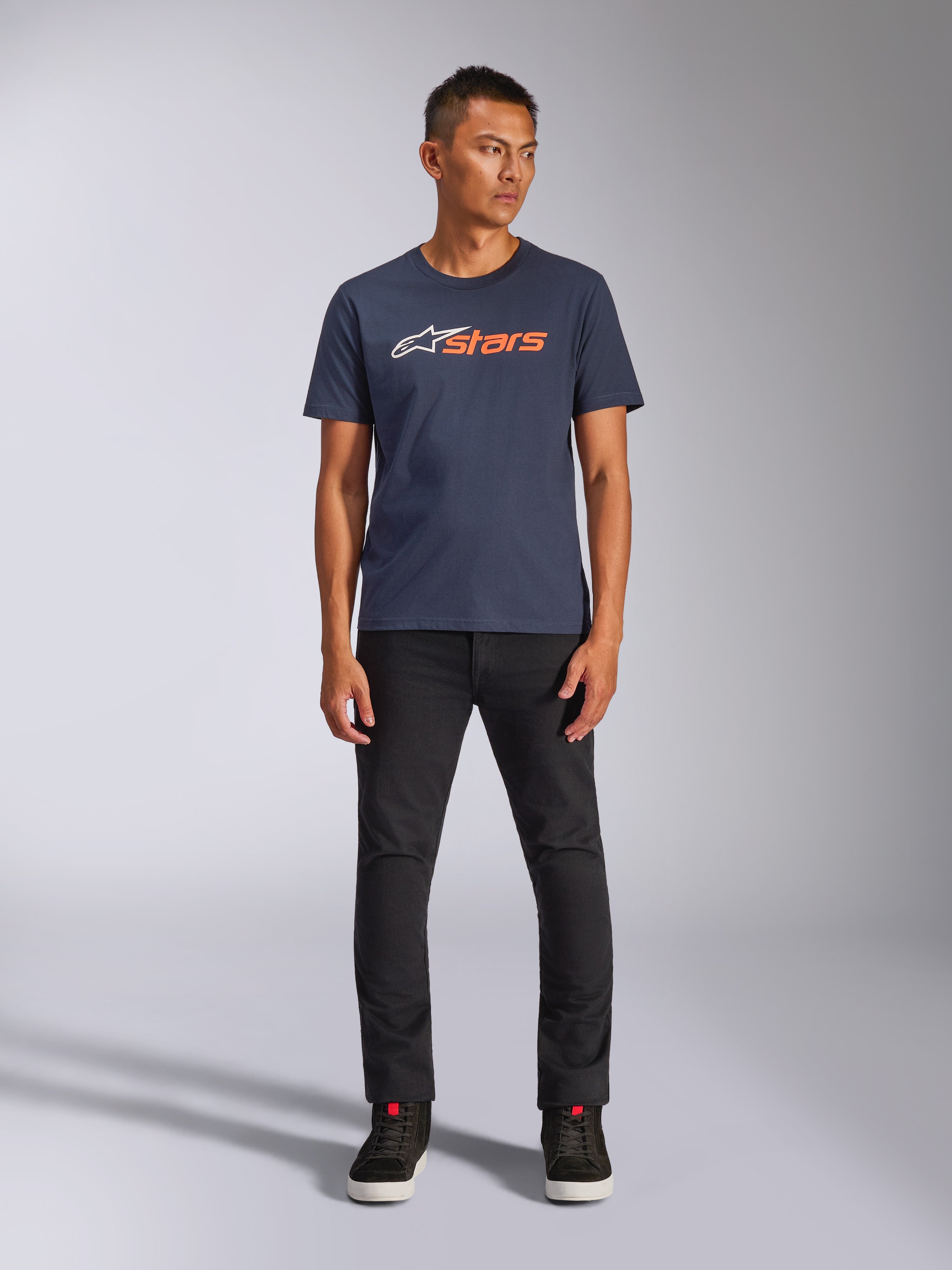 T-shirt Alpinestars Blaze 2.0 CSF, t-shirt à manches courtes, bleu marine avec logo Astars blanc et orange, porté avec un pantalon noir et des baskets noires, streetwear décontracté d'inspiration sport mécanique