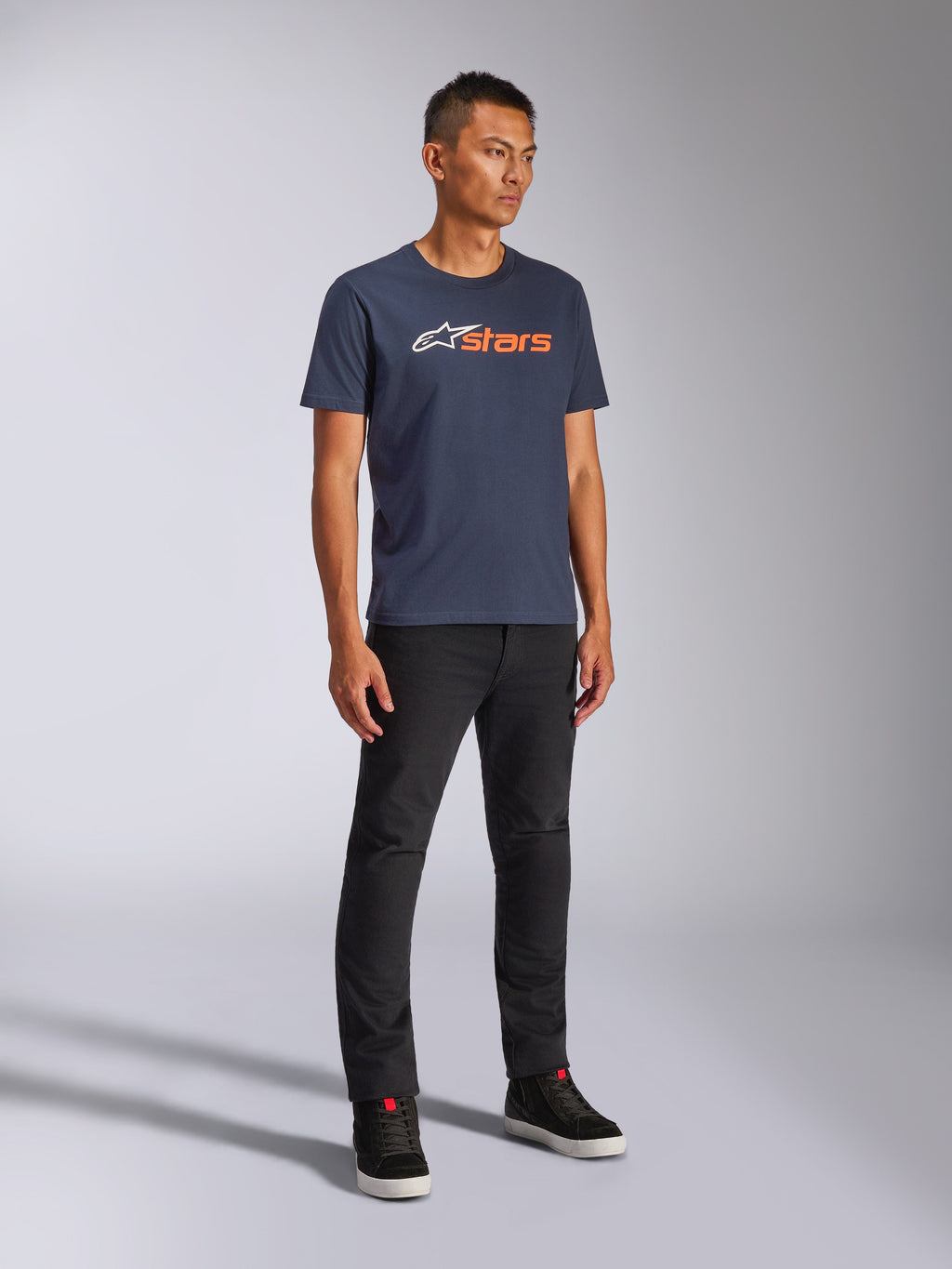 T-shirt Alpinestars Blaze 2.0 CSF, t-shirt à manches courtes, bleu marine avec logo Blaze blanc et orange, porté par un mannequin avec un pantalon noir et des baskets, streetwear décontracté inspiré du sport automobile