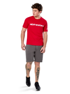 T-shirt Alpinestars Linear Wordmark 2.0 CSF, t-shirt à manches courtes, rouge avec logo mot-symbole blanc sur la poitrine, porté par un mannequin avec un short gris et des baskets noires, streetwear décontracté d'inspiration sport automobile