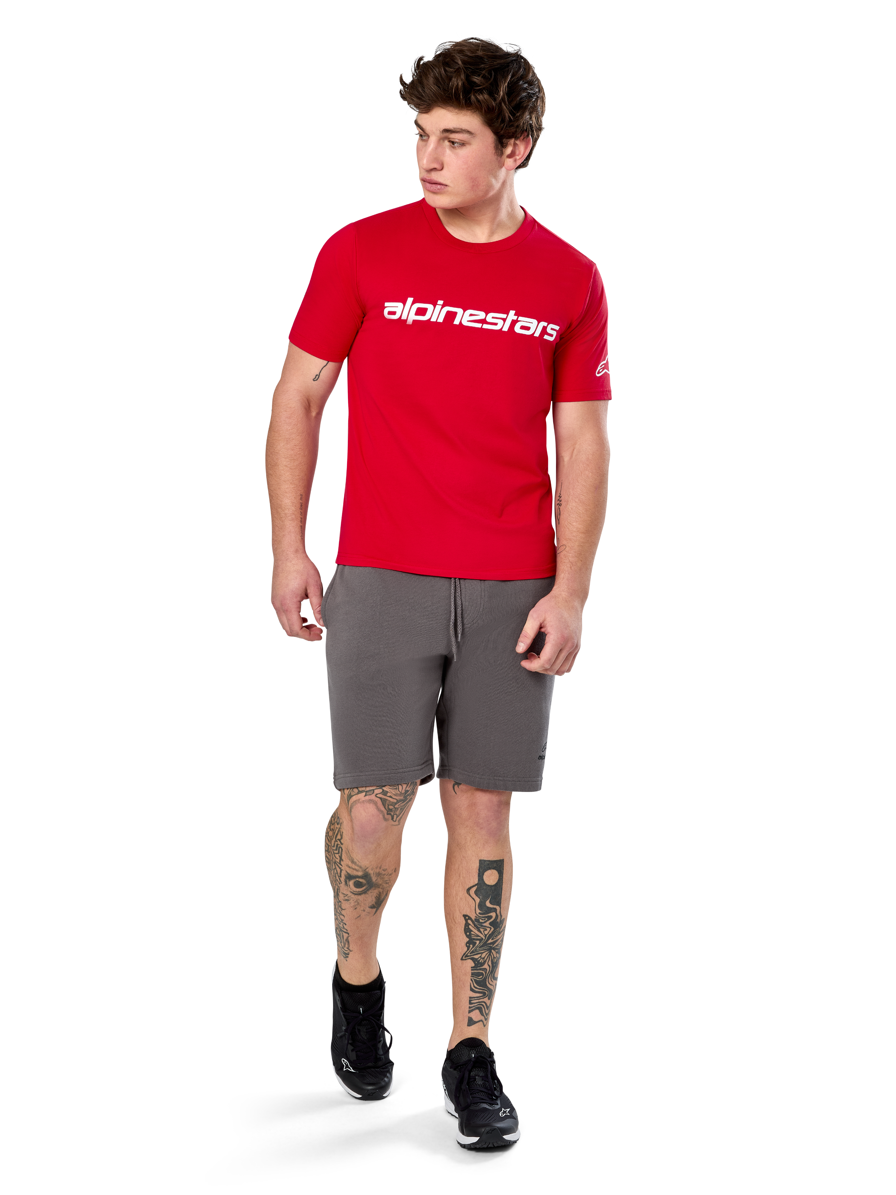 T-shirt Alpinestars Linear Wordmark 2.0 CSF, t-shirt à manches courtes, rouge avec logo mot-symbole blanc sur la poitrine, porté par un mannequin avec un short gris et des baskets noires, streetwear décontracté d'inspiration sport automobile