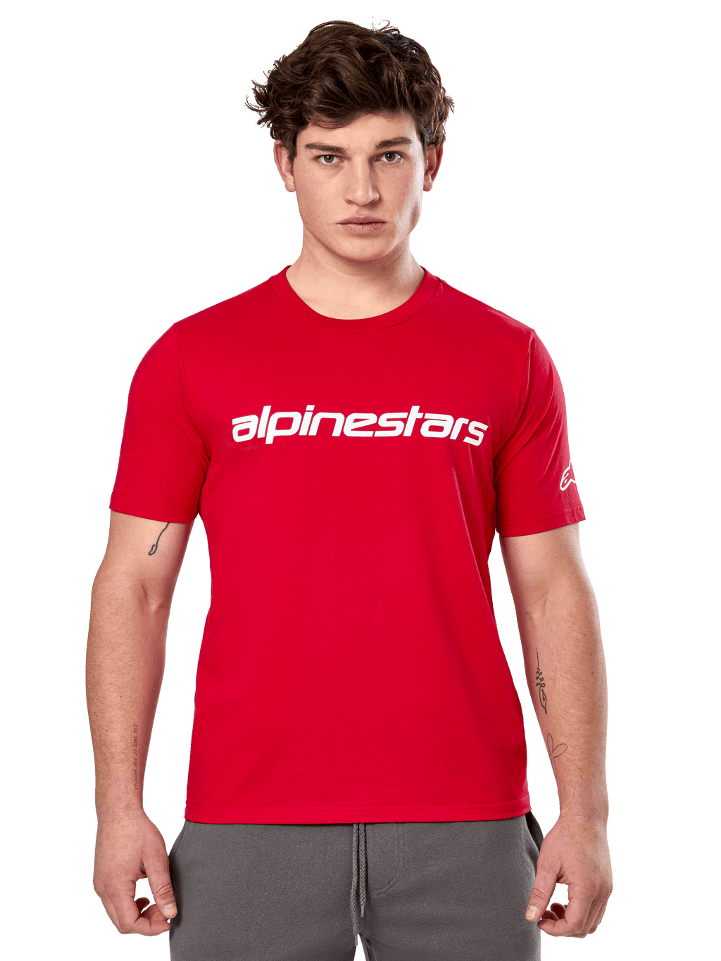 T-shirt Alpinestars Linear Wordmark 2.0 CSF, t-shirt à manches courtes, rouge, mot-symbole linéaire blanc sur la poitrine et logo Ageless sur la manche, porté par un mannequin homme avec un pantalon de survêtement gris, style streetwear décontracté inspiré du sport automobile