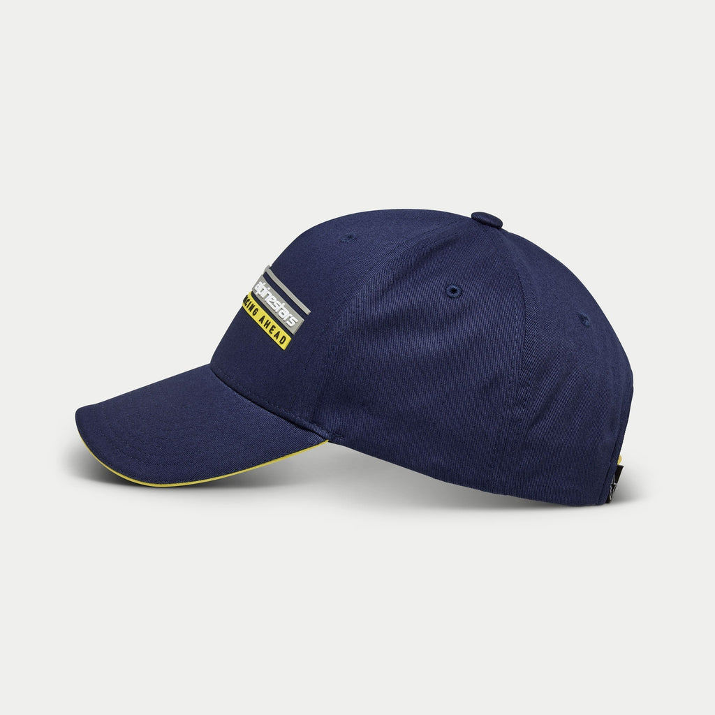Casquette Alpinestars Par, casquette de baseball bleu marine, vue de profil, couronne structurée avec visière courbée et détail sandwich jaune, broderie 3D du logo linéaire Alpinestars Racing Ahead, couvre-chef décontracté inspiré des sports mécaniques