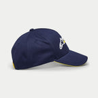 Alpinestars Par Hat, casquette de baseball bleu marine, vue de profil montrant le logo brodé blanc et jaune, visière courbée avec bordure sandwich jaune, couvre-chef structuré décontracté