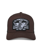 Casquette Trucker Heritage Patch Alpinestars, devant marron avec arrière en maille noire, visière courbée et couronne structurée, grand écusson brodé avec roue ailée et graphisme « Racing Ahead », couvre-chef décontracté inspiré du sport automobile