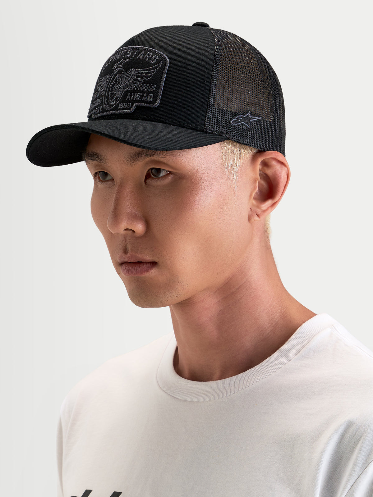 Alpinestars Casquette Trucker Heritage Patch, casquette de sport décontractée, noire et grise, visière courbée et couronne structurée avec écusson brodé sur le devant, portée par un modèle