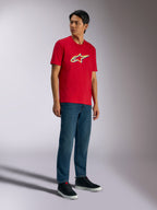 T-shirt Alpinestars Ageless Shadow CSF, T-shirt à manches courtes, rouge, avec le logo Ageless Shadow aux accents jaunes et bleus, porté par un mannequin avec un jean en denim et des baskets noires, streetwear motorsport décontracté
