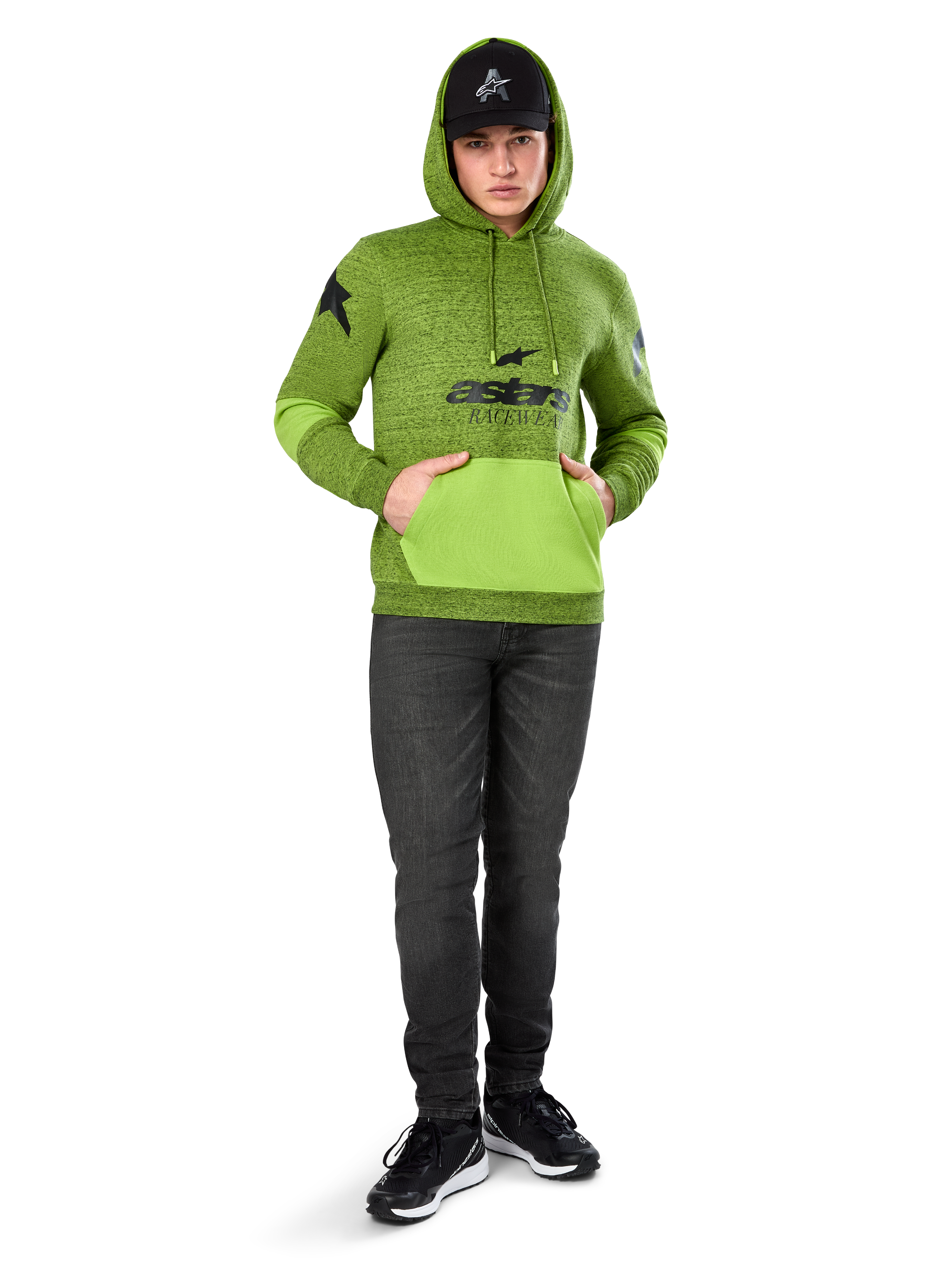 Sweat à capuche Perpetuate Alpinestars, molleton chiné vert lime avec poche kangourou et empiècements aux manches vert vif contrastants, graphisme 'astars' noir sur le devant, porté avec une casquette noire et un jean foncé, streetwear décontracté inspiré du sport automobile