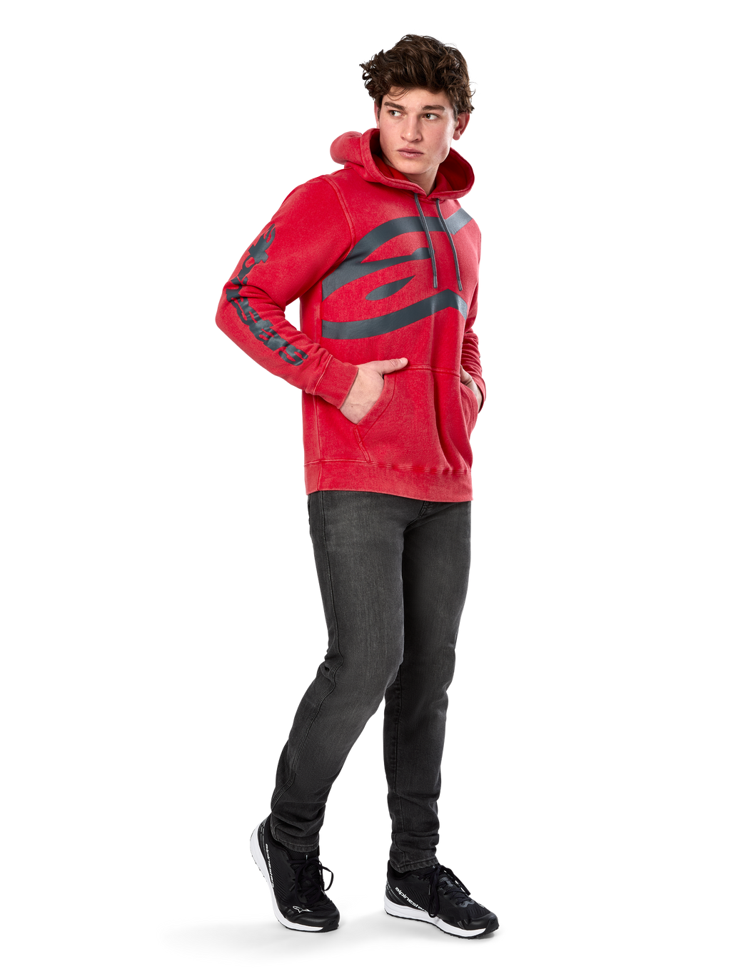Sweat à capuche Alpinestars Unbound, polaire rouge teint en vêtement, très grand logo sombre sur la poitrine et marquage sur les manches, poche kangourou, capuche à cordon de serrage, porté par un mannequin avec un jean gris foncé et des baskets noires, streetwear décontracté inspiré du sport automobile