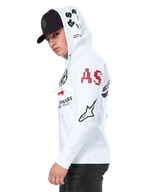 Alpinestars Variegate Hoodie, White zip-front fleece hoodie, multi-logo artwork on the sleeves and hood featuring red 'AS' lettering and black star logo, worn by a man with a black cap, casual motorsport streetwear