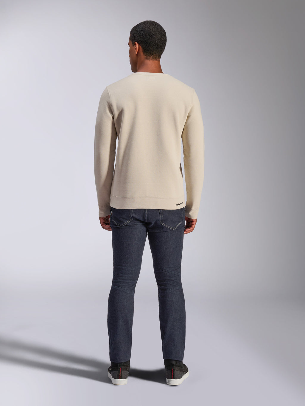 Sweatshirt Alpinestars Positive Crew, Off White, vue arrière d'un homme portant un pull beige à col rond avec ourlet et poignets côtelés, associé à un jean foncé, streetwear décontracté inspiré du sport automobile.
