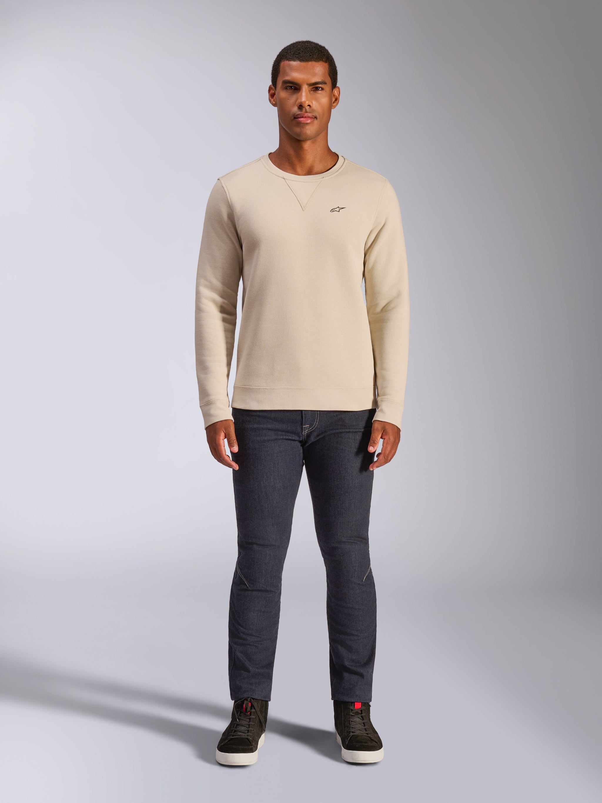 Alpinestars Positive Crew, sweatshirt à col rond blanc cassé, petit logo noir sur la poitrine, poignets et ourlet en bord-côte, surpiqûres en triangle au col, streetwear décontracté porté avec un jean foncé