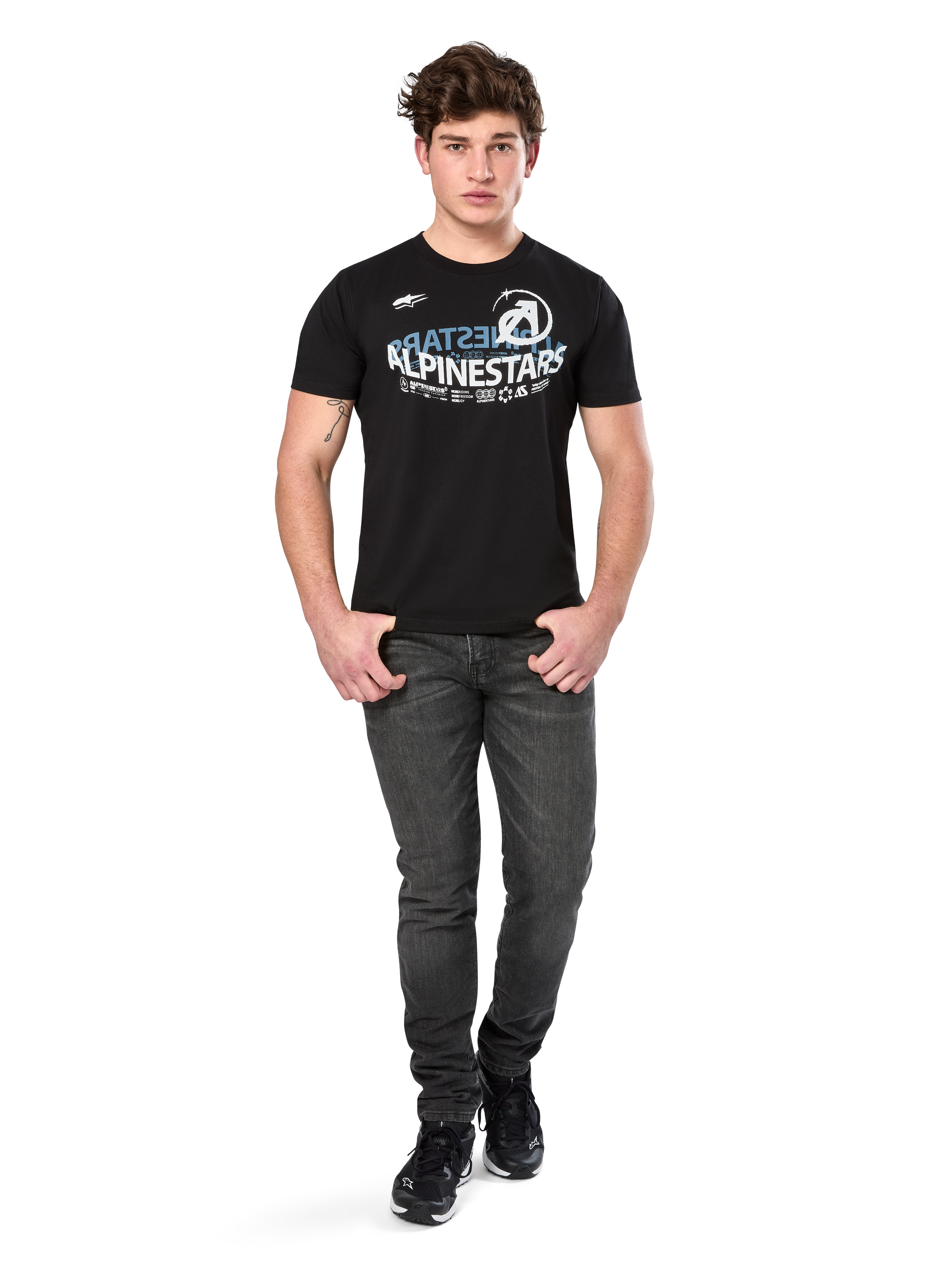 T-shirt Alpinestars Semicircle CSF, t-shirt à manches courtes, noir, graphique incurvé blanc et bleu clair sur la poitrine, porté par un mannequin avec un jean gris foncé et des baskets noires, streetwear motorsport décontracté