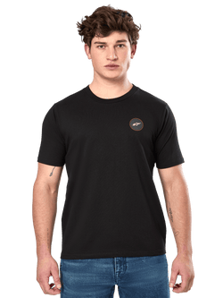 Alpinestars Dot Carbon CSF Tee, t-shirt à manches courtes, noir, petit logo circulaire sur la poitrine avec Astar blanc et bordure rouge, porté par un mannequin avec un jean bleu, style streetwear motorsport décontracté