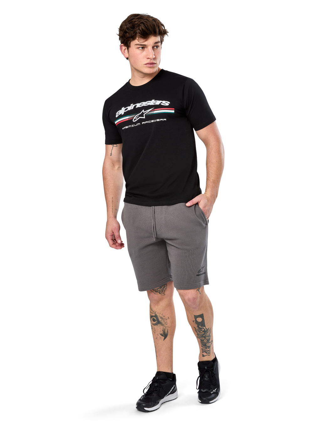 Alpinestars Prevail Csf Tee, t-shirt à manches courtes, noir, logo Alpinestars blanc avec rayure paddock tricolore, porté avec un short gris et des baskets noires, streetwear motorsport décontracté