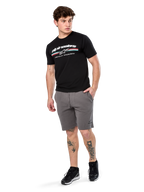 Alpinestars Prevail Csf Tee, t-shirt à manches courtes, noir, logo Alpinestars blanc avec rayure paddock tricolore, porté avec un short gris et des baskets noires, streetwear motorsport décontracté