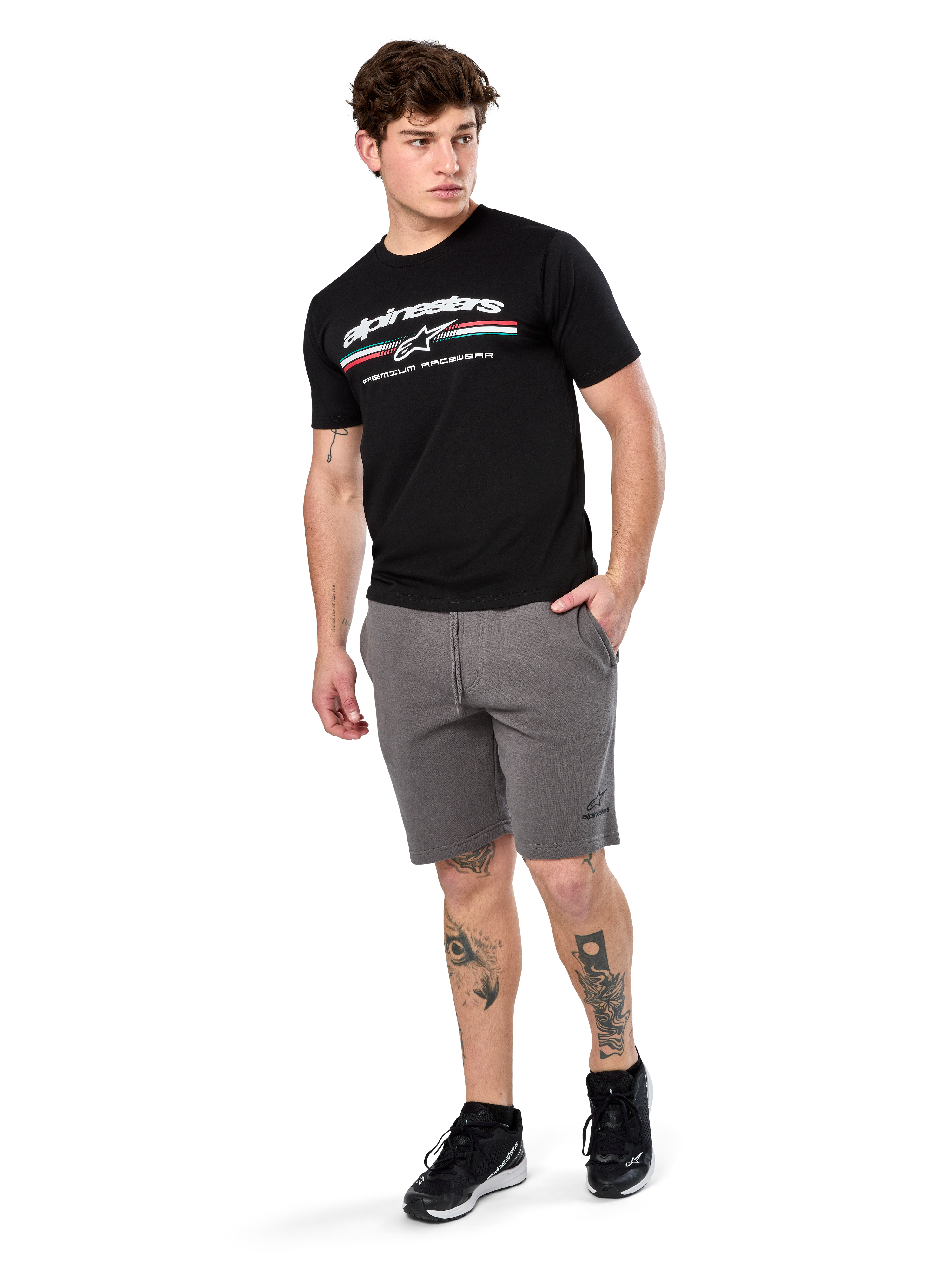 Alpinestars Prevail Csf Tee, t-shirt à manches courtes, noir, logo Alpinestars blanc avec rayure paddock tricolore, porté avec un short gris et des baskets noires, streetwear motorsport décontracté