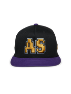 Casquette Alpinestars Franchise, casquette noire et violette à visière plate, couronne structurée avec visière et bouton supérieur violets, logo « AS » doré brodé en 3D à l'avant, streetwear décontracté inspiré du sport automobile