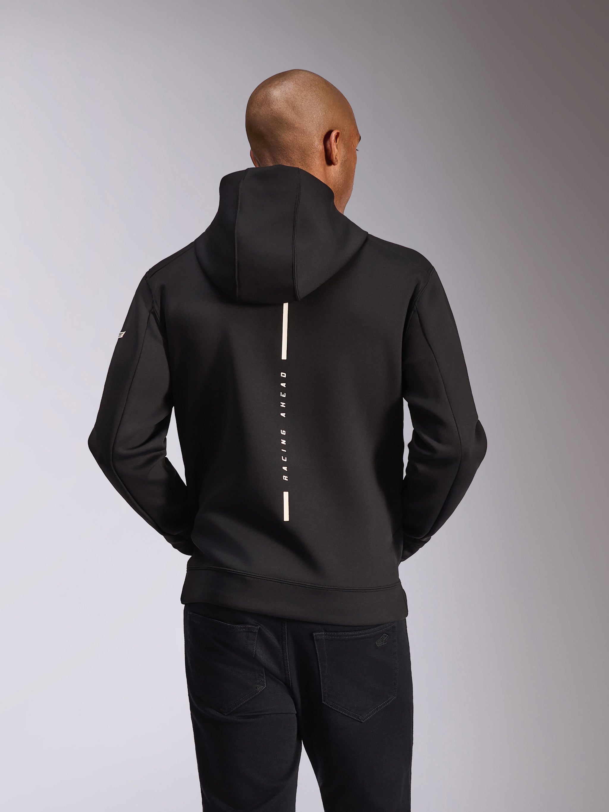 Alpinestars Insight Hoodie, back view, Black, vertical white stripe with 'RACING AHEAD' text, sleeve wordmark branding, casual motorsport-inspired streetwear
