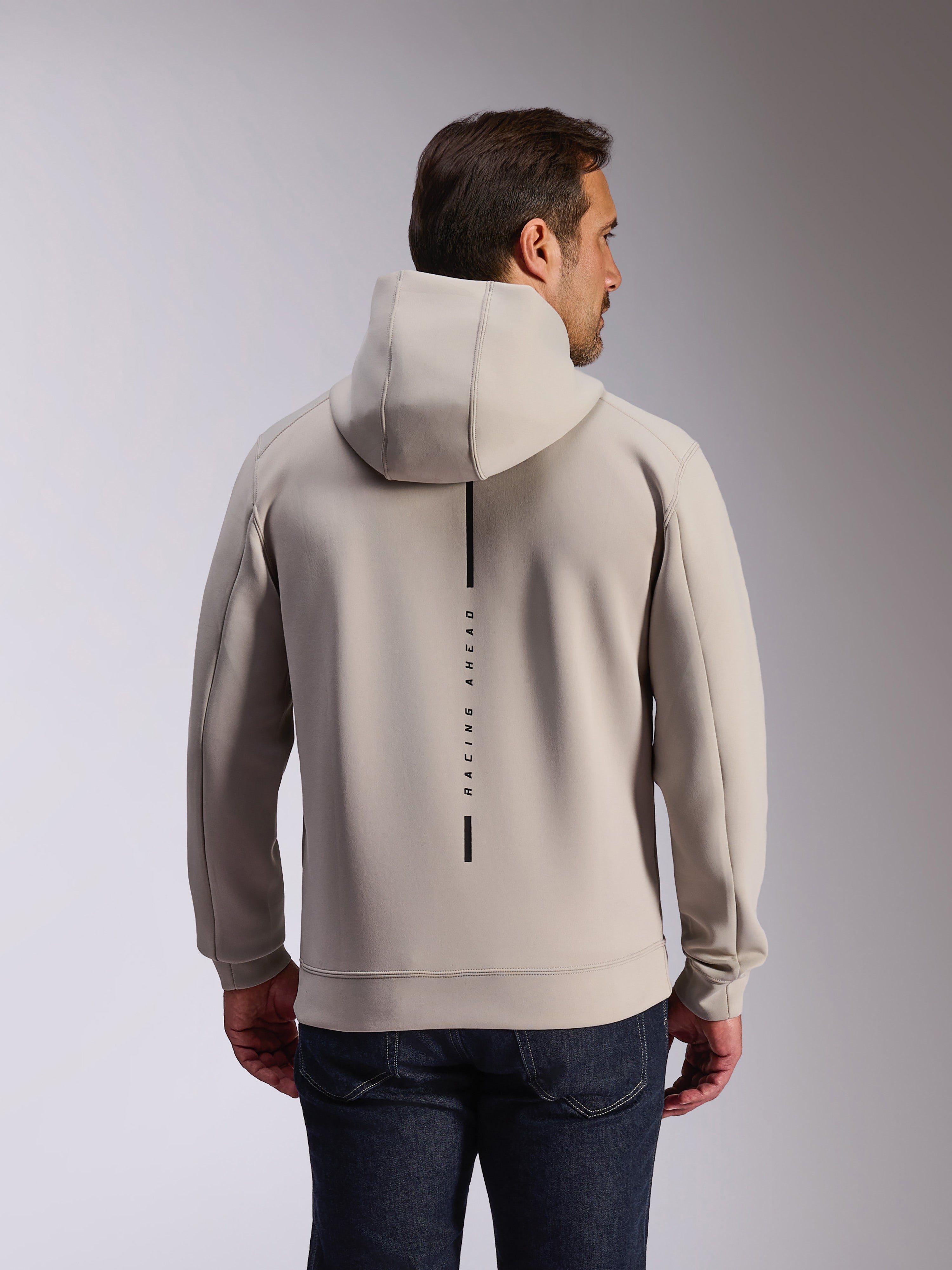 Sweat à capuche Alpinestars Insight en Cement, vue arrière d'un mannequin portant un sweat-shirt gris clair, présente un logo à bande verticale noire avec l'inscription 'RACING AHEAD', sweat à capuche décontracté en polaire double face inspiré du sport automobile.
