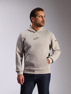 Sweat à capuche Alpinestars Insight, sportswear décontracté, gris ciment, modèle à enfiler avec poche kangourou et petit logo Astars noir sur la poitrine, manches longues avec logo Alpinestars sur le bras gauche, porté par un mannequin avec un jean en denim foncé, vêtements lifestyle inspirés du sport automobile
