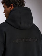 Sweat à capuche Alpinestars Emergent Oversized, vêtement streetwear décontracté noir, vue de dos avec logo Alpinestars en lettres brodées 3D, coupe ample et texture polaire premium