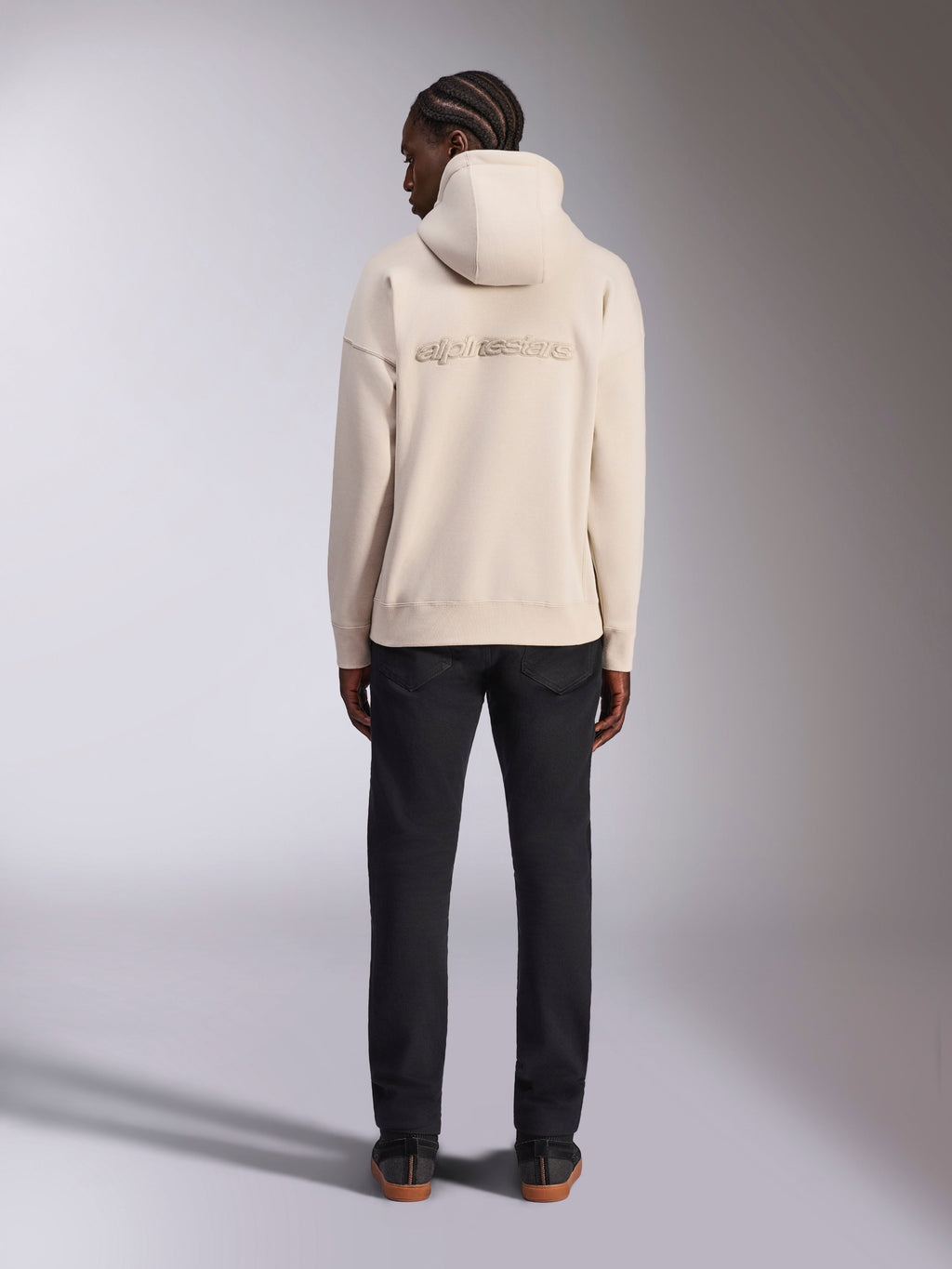 Sweat à capuche Oversized Emergent Alpinestars, blanc cassé, vue de dos avec logo Alpinestars brodé en 3D, sweat en polaire coupe ample, associé à un pantalon noir, design streetwear décontracté
