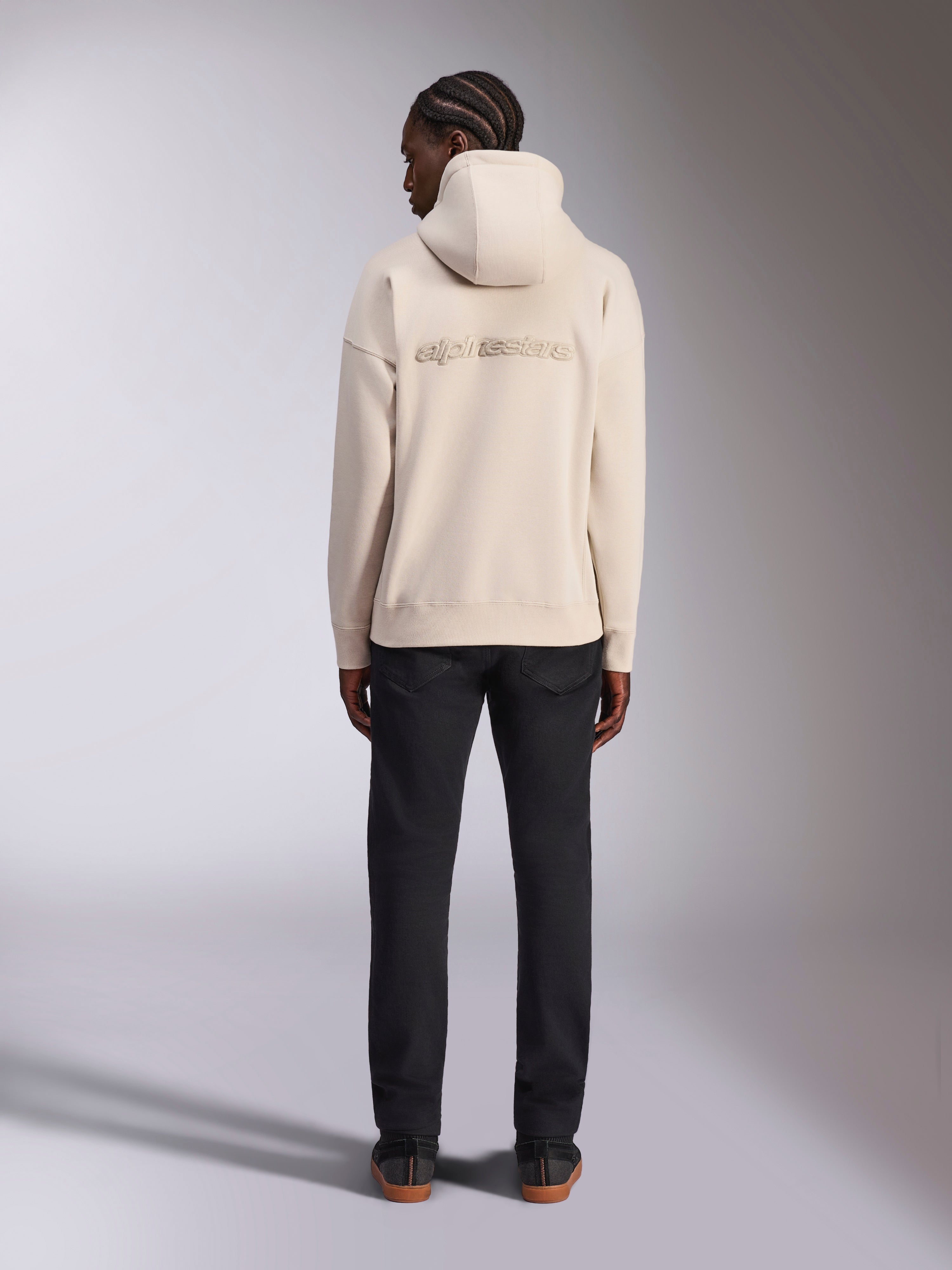 Sweat à capuche Oversized Emergent Alpinestars, blanc cassé, vue de dos avec logo Alpinestars brodé en 3D, sweat en polaire coupe ample, associé à un pantalon noir, design streetwear décontracté