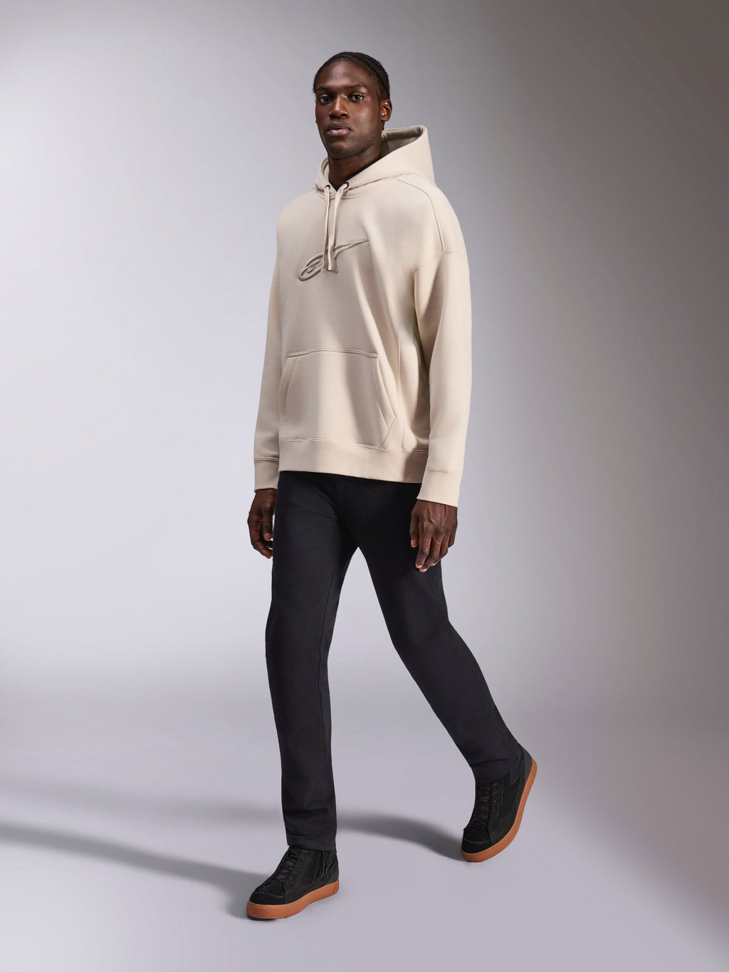 Sweat à capuche oversized Alpinestars Emergent, streetwear décontracté, blanc cassé, logo brodé en 3D ton sur ton, porté par un mannequin avec pantalon noir et baskets noires, coupe ample avec poche kangourou et capuche à cordon de serrage