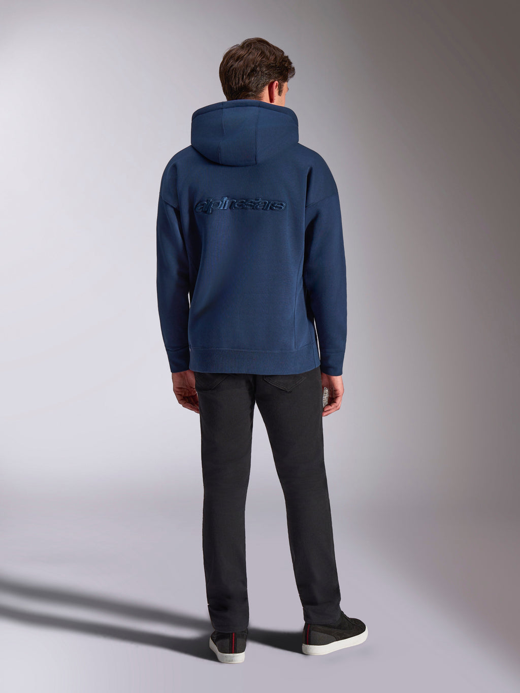 Sweat à capuche Alpinestars Emergent Oversized, streetwear décontracté, bleu marine, logo Alpinestars brodé ton sur ton au dos, coupe oversized avec capuche, porté avec un pantalon noir, vue de dos