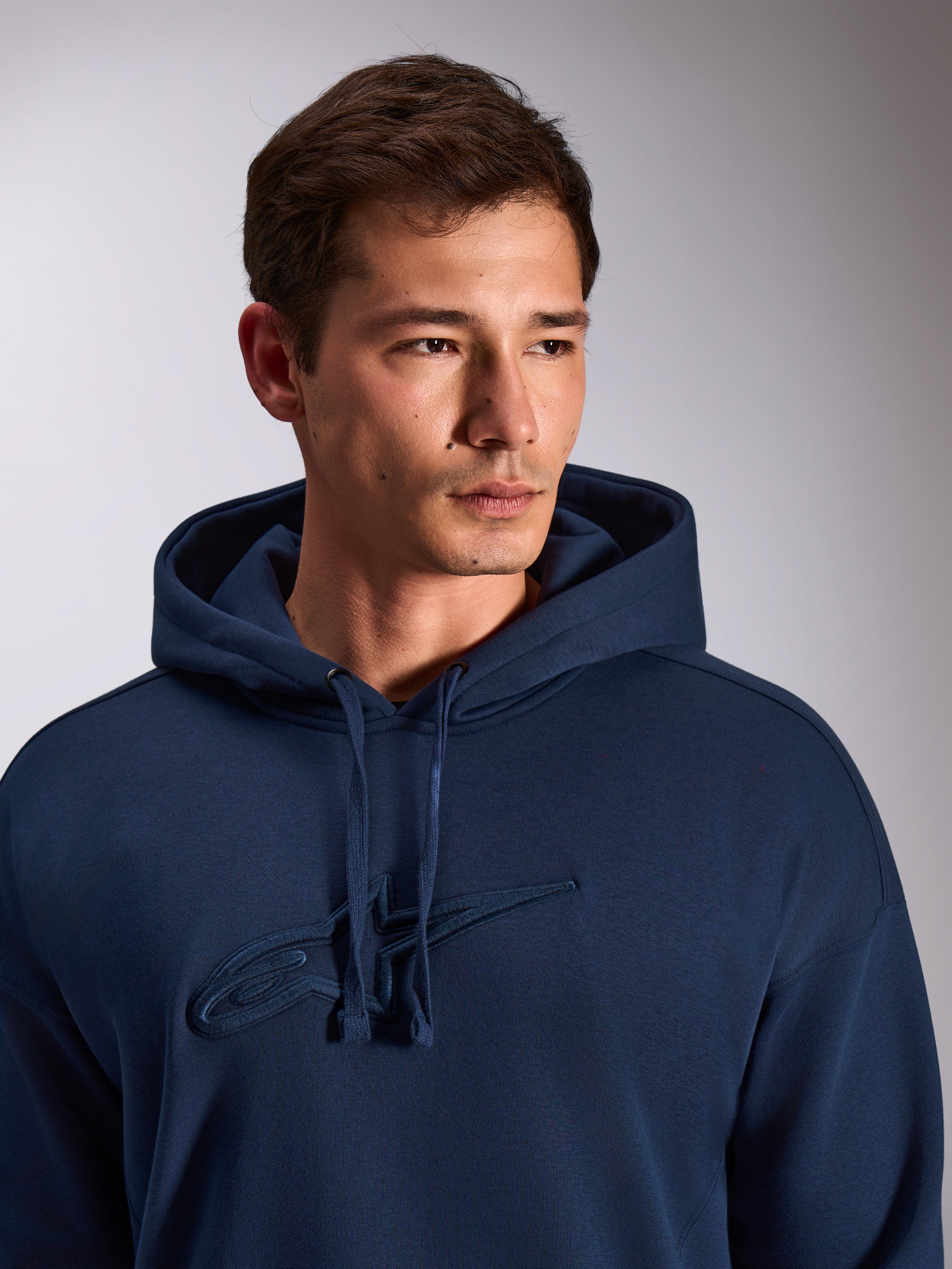 Alpinestars Emergent Oversized Hoodie, bleu marine, gros plan d'un mannequin portant un sweat à capuche en polaire, logo Astars brodé en 3D ton sur ton sur la poitrine, capuche à cordon de serrage réglable, style streetwear décontracté