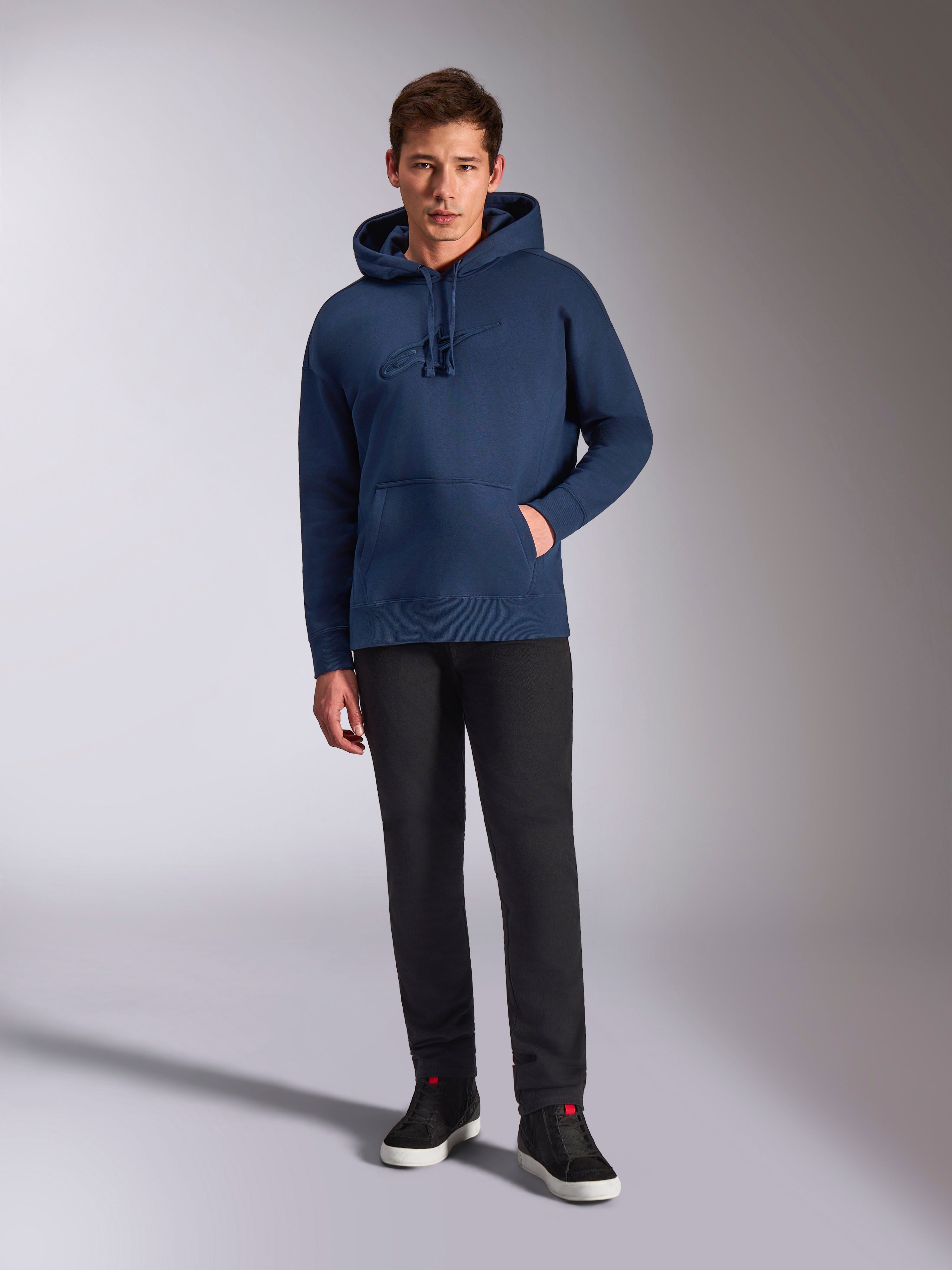 Alpinestars Emergent Oversized Hoodie, sweat à capuche en polaire bleu marine, logo brodé en 3D ton sur ton sur le devant, porté par un mannequin avec un pantalon noir et des baskets, style streetwear décontracté
