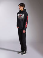 Sweat à capuche Alpinestars Obsessed, sweat en polaire noir à enfiler, avec un grand graphisme blanc moucheté sur la poitrine, logo Astars rouge et marquage rouge sur la manche, porté par un mannequin avec pantalon noir et baskets, style streetwear motorsport décontracté