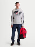 Alpinestars Sweat À Capuche Obsessed, sweat de sportswear en polaire pour homme, gris ciment avec graphismes dégradés rouges et noirs d'inspiration MX, logos sur les manches, porté par un modèle tenant un sac à dos Alpinestars rouge.