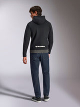 Sweat à capuche Parallel Alpinestars, vue de dos d'un homme portant un sweat en polaire à enfiler noir et anthracite, logo Alpinestars blanc dans le bas du dos, associé à un jean bleu foncé, style streetwear décontracté inspiré des sports mécaniques
