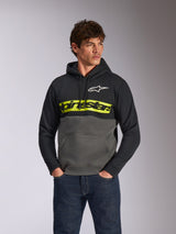 Sweat à capuche Parallel Alpinestars, polaire décontractée avec design en blocs de couleurs, noir et gris anthracite avec une bande jaune vif sur la poitrine, logo Alpinestars textuel et logo étoile blanc, porté par un modèle masculin avec un jean bleu foncé