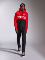 Sweat à capuche Parallel Alpinestars, polaire à enfiler en blocs de couleurs rouge et noir, logo textuel Alpinestars blanc sur la poitrine et logo Astars sur la poitrine gauche, porté par un mannequin avec un pantalon noir et des baskets montantes, style streetwear décontracté