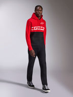 Sweat à capuche Alpinestars Parallel, sportswear décontracté, design à blocs de couleurs rouge et noir, avec lettrage blanc et logo étoilé Alpinestars sur la poitrine, porté avec un pantalon noir et des baskets, look moderne inspiré des sports mécaniques