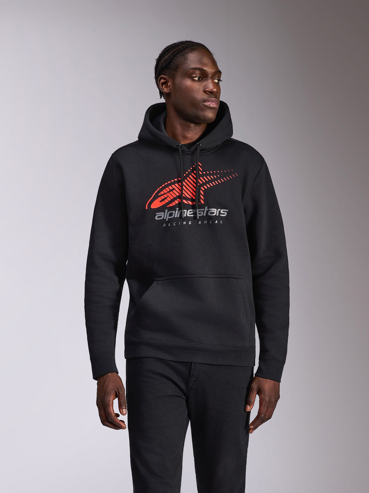 Alpinestars Pulse Hoodie, sweat à capuche décontracté à enfiler, noir avec logo Astars rouge et gris présentant une ligne de vitesse dégradée et le texte « Racing Ahead », capuche avec cordon de serrage et poche kangourou, streetwear inspiré du sport automobile porté par un mannequin
