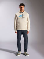 Sweat à capuche Alpinestars Pulse, blanc cassé, pull à manches longues avec capuche à cordon, logo Astars Combo bleu et noir avec dégradé de lignes de vitesse, porté avec un jean foncé et des baskets, style streetwear motorsport décontracté