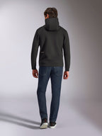 Alpinestars Cypher Hoodie, black double-face fleece, back view showing a small white Alpinestars logo on the lower left hip, high-neck hood, paired with dark blue jeans, casual motorsport-inspired streetwear