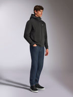 Alpinestars Cypher Hoodie, casual streetwear, black zip-up hoodie, male model wearing with dark blue jeans and black sneakers, high-neck hood with Alpinestars word logo, small white Astars logo on chest, sleek motorsport-inspired lifestyle look
