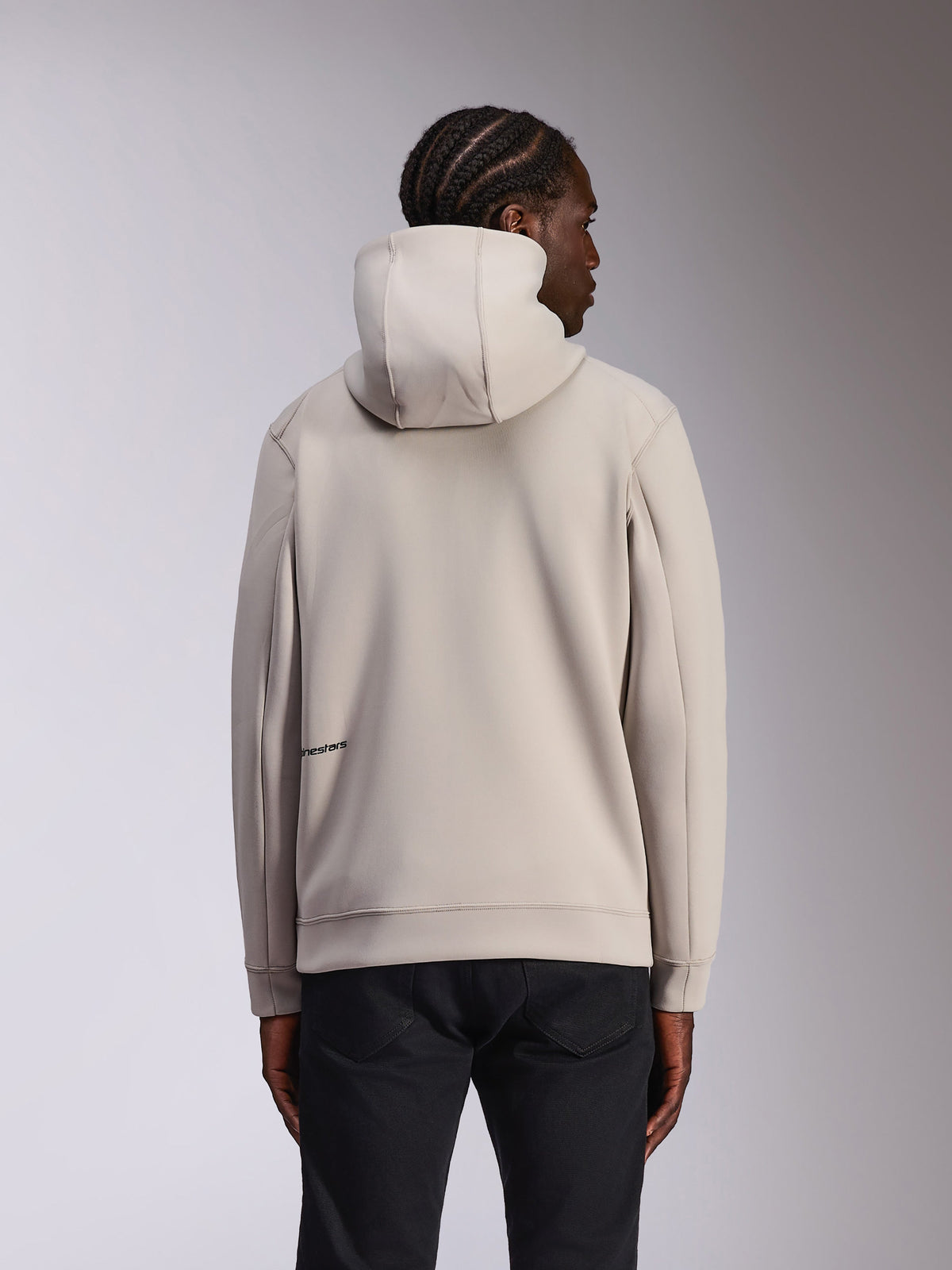 Sweat à capuche Alpinestars Cypher, sportswear décontracté, gris Cement, vue de dos sur modèle, capuche à col haut, matière polaire double face, logo Alpinestars discret dans le bas du dos, porté avec un pantalon noir